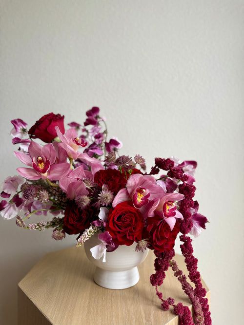 Bouquet of pink and red flowers in a white vase on a wooden surface with a light gray background